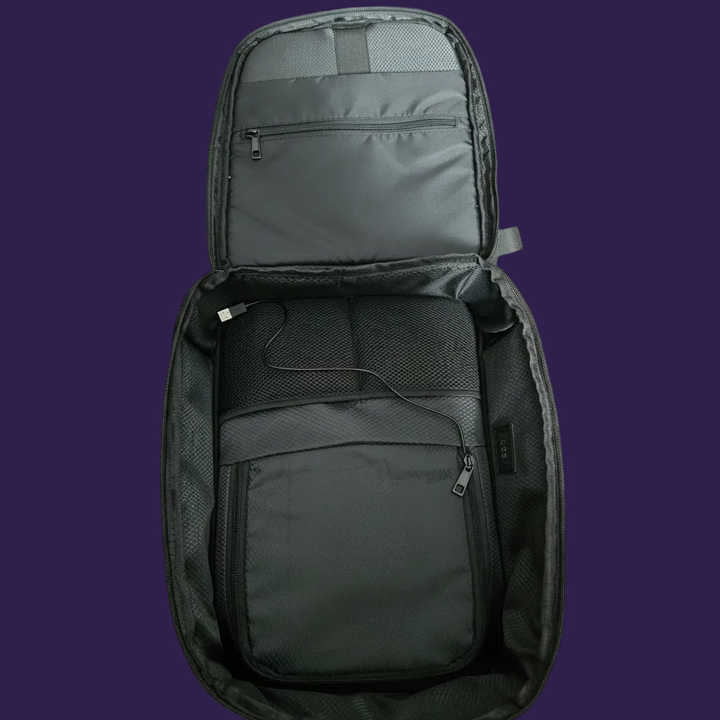 An open black backpack shown from above, revealing its interior compartments, mesh pockets, and padded organizer, placed on a textured carpet.