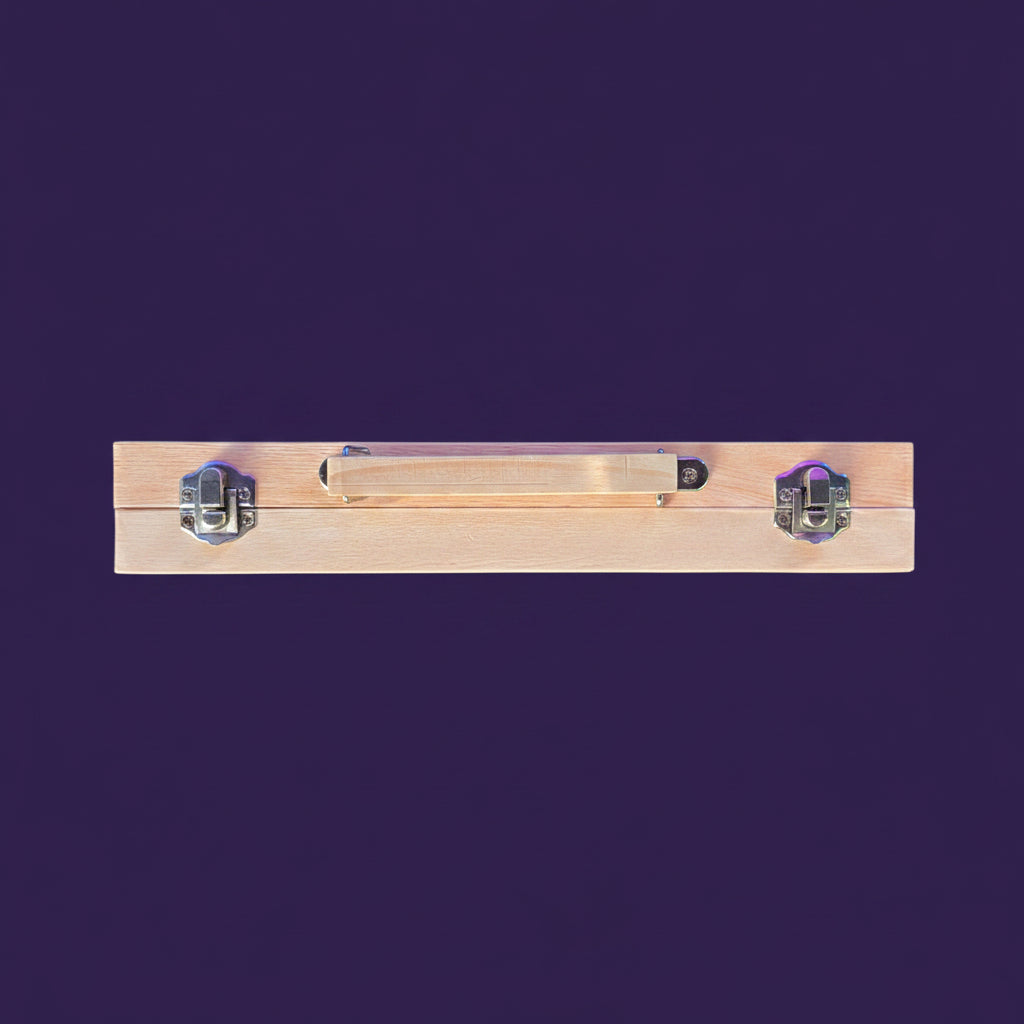 A light wood rectangular case or box with a metal handle and two silver metal clasps, photographed from above on a dark ribbed surface with part of a person's legs visible at the bottom.