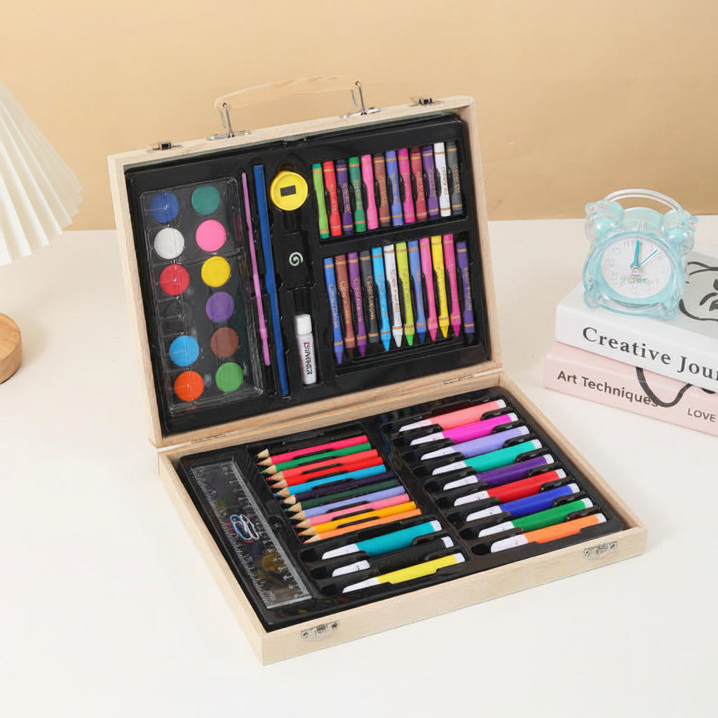 A wooden carrying case opened to show a comprehensive art and craft set, including watercolor paints, colored pencils, markers, a ruler, and other drawing tools, displayed on a white table next to decorative props.