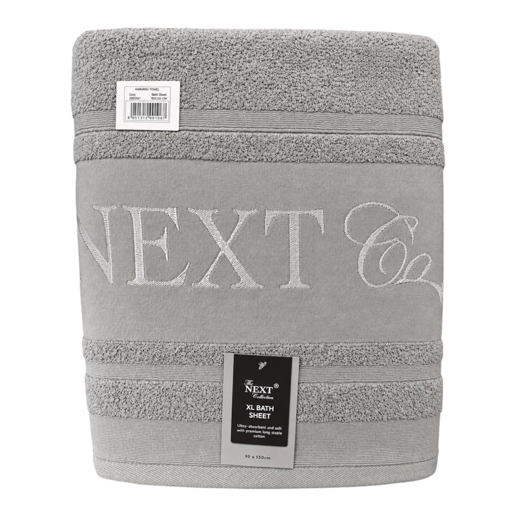 A folded gray bath sheet with 'NEXT Co' embroidered in light gray on the front, featuring textured stripe bands and a black product label.