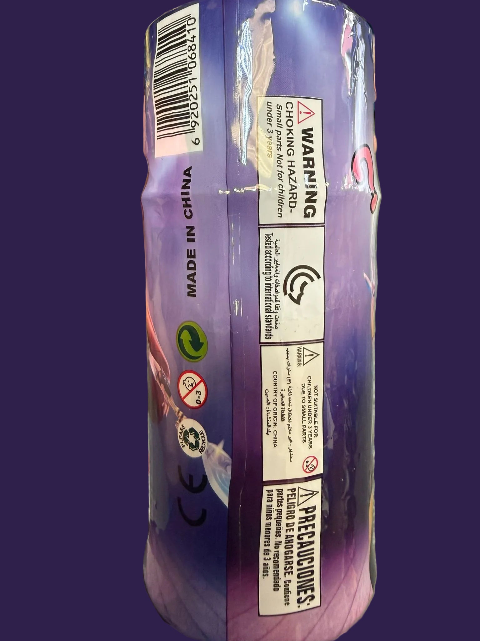 Hand holding a purple product package with various labels and warnings.
